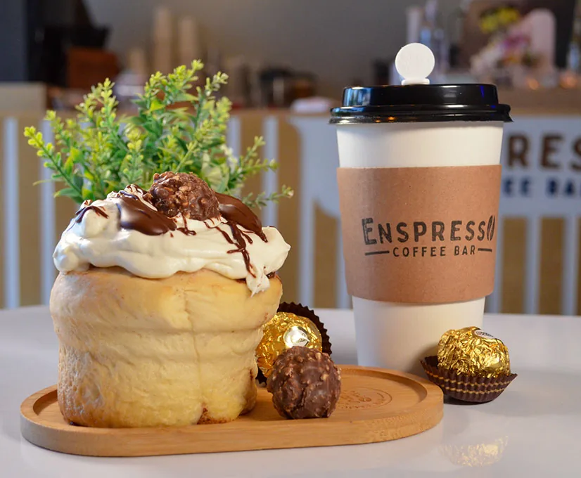 Rol con crema, chocolate y bombones junto a un café caliente
